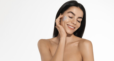 Tender young woman with eyes closed, gentle smile, touches her soft cheek, enjoys feeling of softness after skincare moisturizer, soothing hydration cream and serum, white studio background © Liubov Levytska