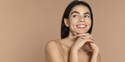 Wellness and women concept. Beautiful young woman with glazy donut skin, glowy face without blemishes, zero imperfections, smiling and looking happy, gazing at empty space on banner, brown background © Liubov Levytska