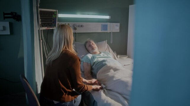 Elderly man rests on pillow and concerned woman sits nearby