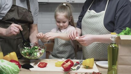 A child helps parents prepare fresh vegetables in the kitchen. The family enjoys cooking together, creating a warm atmosphere, learning, and strengthening their bond. 