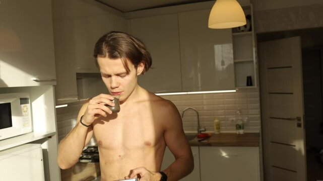 a man with a naked torso drinks puer tea in the kitchen in the morning