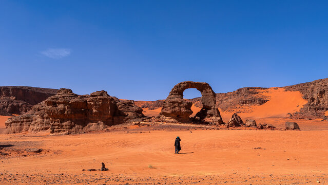 One person and Arch in Tadrart Rouge, meaning Red Mountain, a mountain range in southeastern Algeria, part of the Algerian Desert providing massive dunes, rock formations and Martian landscapes