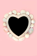 Heart shape mother of pearl seashell wreath with wooden frame on pink background and chalkboard....