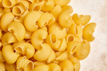 High-resolution close-up of uncooked yellow pipe rigate pasta with ribbed, curved forms arranged in...