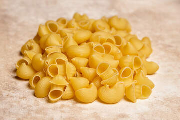 Low-angle view of uncooked yellow pipe rigate pasta with ribbed, hollow curves piled on a textured...