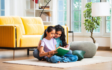 Happy Indian Asian mom and daughter bonding while reading a book on the floor at home