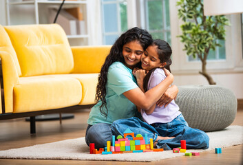 Asian child and mother making colorful house using wooden toys while sitting indoors at home