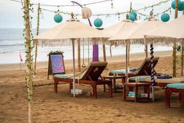 Tranquil Bali beach scene with sunbeds shaded by umbrellas. Turquoise accents and hanging lanterns...