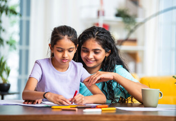 Little Indian girl draws with pastel crayons as mother supports and praises her creativity