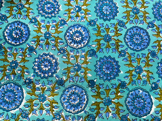 An intricate dark blue floral pattern with lush green leaves is hand block printed on rich blue...
