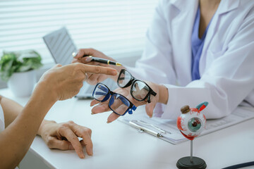 A female doctor talks to an elderly patient who is being shown a modern eye model in a hospital.