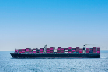 Large, fully loaded, cargo container ship sailing through calm, blue Indian Ocean. International trade route.