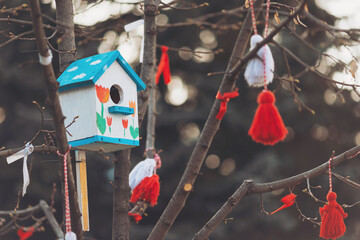 Colorful birdhouse hanging in a decorated tree captures the essence of joy and life during the festive season. Bulgarian traditional spring decor Martenitsa on the tree. Romanian martisor decoration.