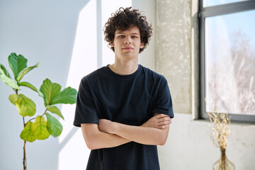 Confident handsome young man with crossed arms in home interior