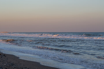 Crystal blue waves roll gently toward the shore under a pastel sky at sunset. The rhythmic movement of the sea creates a serene and calming atmosphere perfect for relaxation and reflection.