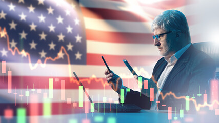 Older businessman analyzing financial charts on two smartphones with a laptop, U.S. flag background, and stock market graphs overlay.