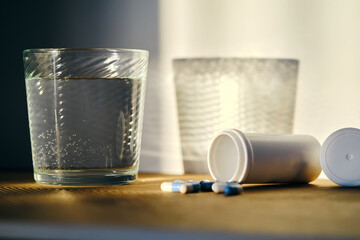 A glass of water and a bottle of pills in the sunlight.