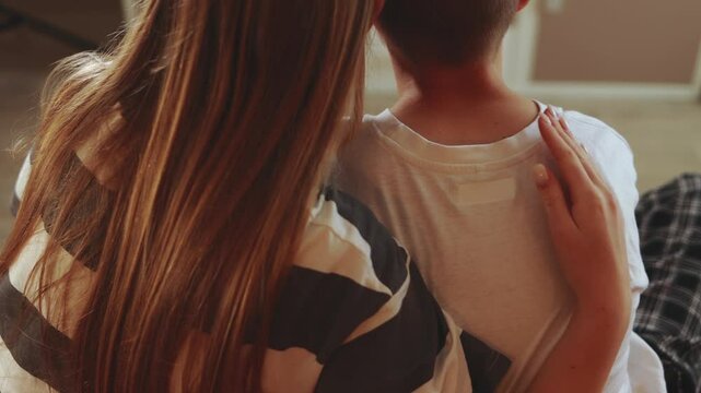 Long-haired older sister providing emotional support, gently embracing younger brother with tender affection, sharing close familial connection and warmth in comfortable home setting