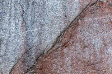 Close-up of a textured rock surface with a mix of gray and reddish-brown hues, featuring natural...