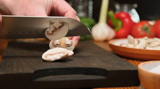 Details: Chef uses a kitchen knife and cutting board to slice fresh champignon mushrooms. Cooking with mushrooms. Vegetarian food.