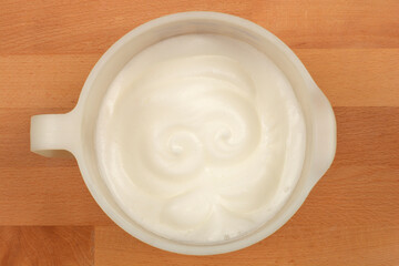 Whipped egg whites, forming a light and airy texture, are in a white oval bowl on a wooden surface