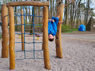 Wooden playground ladder, boy child is hanging upside down from playground bar, outdoor physical activity for kids, motor skill development, active play and exploration