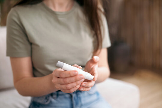 Woman using a glucometer to check blood sugar level at home close-up, concept of diabetes control and self-monitoring.