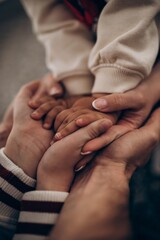 Fototapeta premium Three hands clasped together, child and adult, wearing white sweater and striped sleeves. Soft focus, neutral background. Concept of family, unity, and connection.