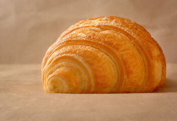 One croissant lying on beige craft paper