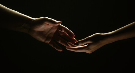 Two hands reaching toward. Helping hand outstretched for salvation on isolated black background. Close up of man and woman hand touch with fingers. Man and woman holding hands.