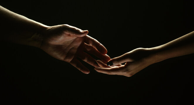 Two hands reaching toward. Helping hand outstretched for salvation on isolated black background. Close up of man and woman hand touch with fingers. Man and woman holding hands.