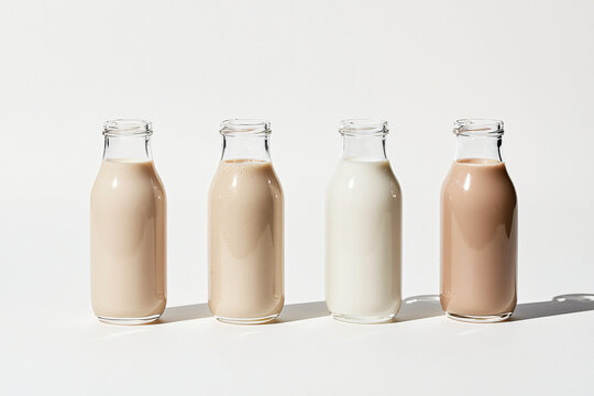 plant milk collection featuring four transparent glass bottles with distinct layers of almond, oat, soy and cashew milk, minimalist white background