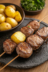 traditional anticuchos de coraz&oacute;n on wooden skewers, charred exterior, served with native potatoes