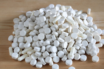 Pile of white pills and capsules forming a small mound on wooden table