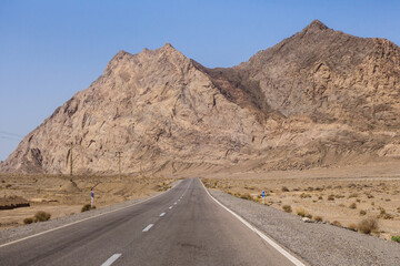 A highway stretching ahead and seemingly dissolving into a suddenly growing high wall of mountains. Shot in Yazd province, Iran