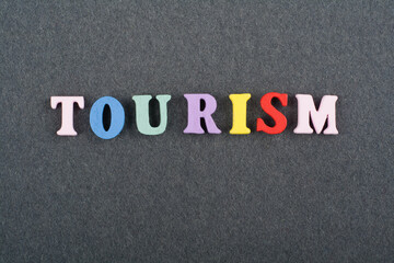 TOURISM word on black board background composed from colorful abc alphabet block wooden letters,...