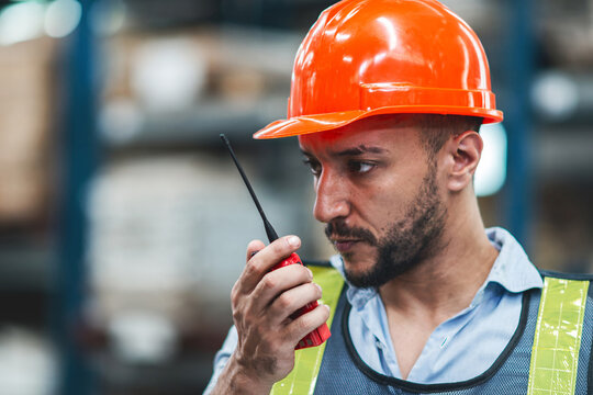 Caucasian worker checking storage using radio. hard work man loading cargo call person to find parcel box in warehouse industry. male supervisor, safely in uniform helmets for protection using talkie