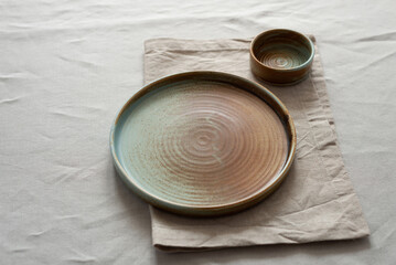 Round plate with a rim in a warm colors on a beige cotton tablecloth. Minimalistic composition with...