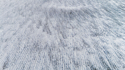 Drone view over a snow covered agriculture field with cultivated rows from crops.