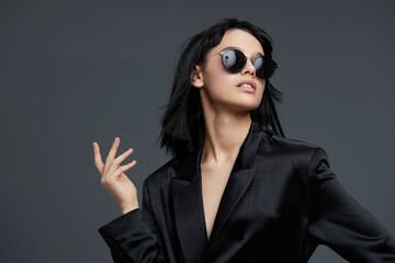 Woman in black suit and sunglasses posing for the camera with one hand on her hip and a finger on...