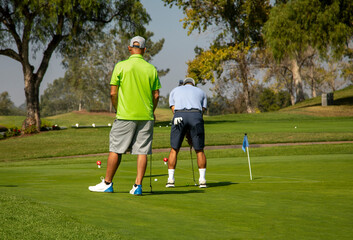 Fototapeta premium A man putting at a practice putting green with another golfer watching