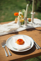 Elegant outdoor place setting with a white plate, light beige napkin, and an orange dahlia