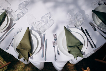 Elegant place setting at a wedding reception with a white tablecloth and a tied sage green napkin...