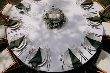 Overhead view of an elegantly set round wedding table with white linens, green napkins, and a floral centerpiece