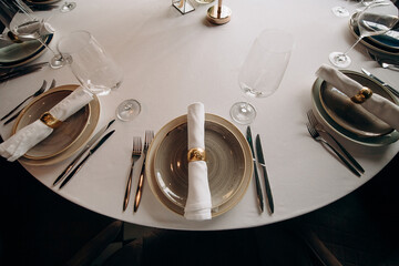 Elegant wedding table setting with white tablecloth, textured plates, white napkins with gold rings, and wine glasses