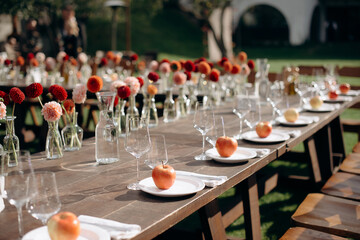 Elegant outdoor wedding table setting with a dark wooden table, white plates, apples as favors, and floral decorations