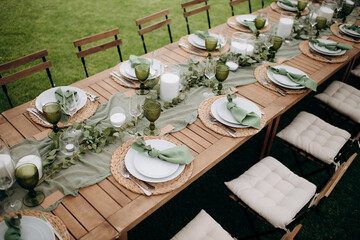 Elegant outdoor wedding table setting with a wooden table, sage green runner, white plates, and...