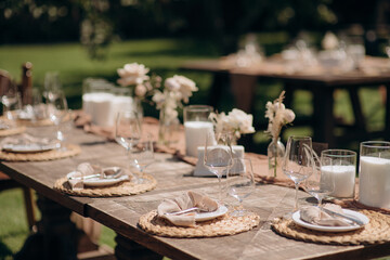 Rustic outdoor wedding table setting with a dark wooden table, beige runner, white plates, and simple floral centerpieces