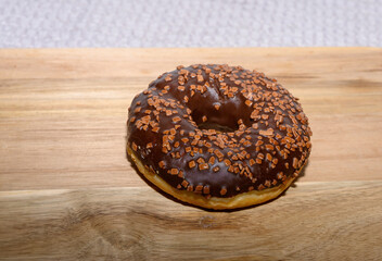 A delectable chocolate donut adorned with crunchy topping sits on a wooden surface, inviting sweet...