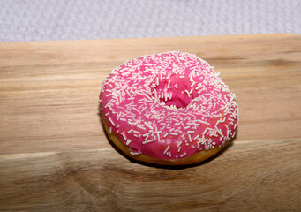 A vibrant pink frosted donut adorned with white sprinkles rests on a light wooden surface, creating...